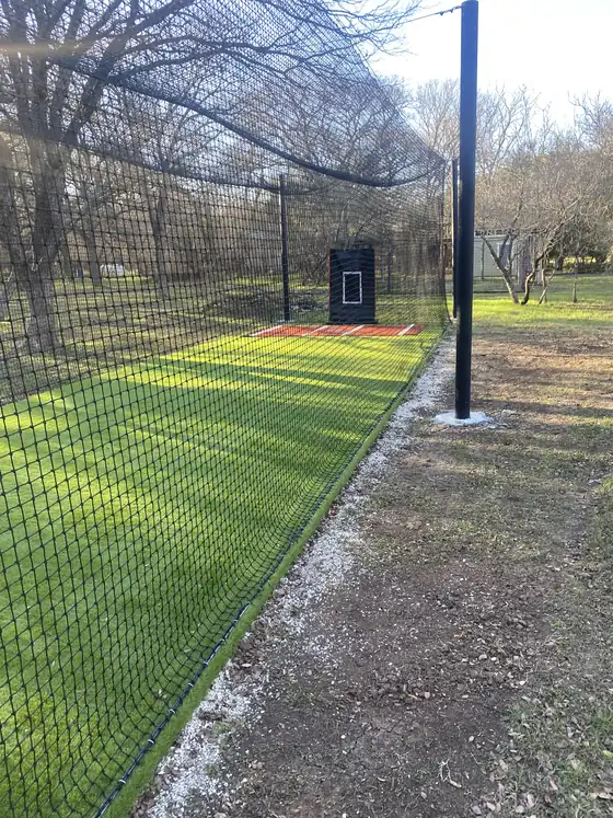 Turf batting cage lane with netting along a fence line
