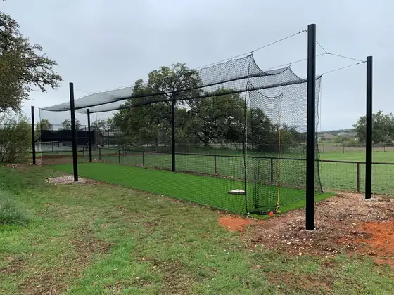 Backyard batting cage with black netting over a turf lane